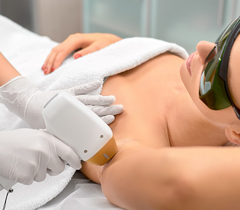 a woman wearing eye protection undergoing a hair removal procedure from a beautician 